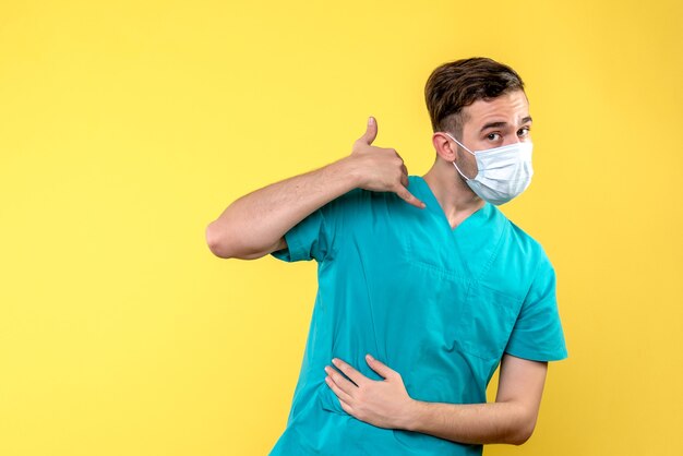 Vista frontal de um médico com máscara estéril na parede amarela