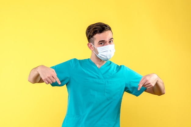 Vista frontal de um médico com máscara estéril na parede amarela