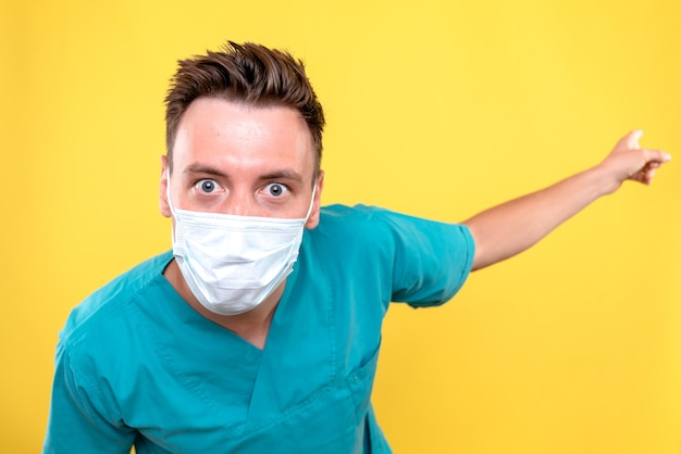 Vista frontal de um médico com máscara estéril na parede amarela