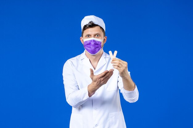 Vista frontal de um médico com uniforme médico e máscara segurando pequenos adesivos médicos em azul