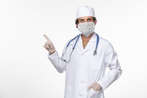 Vista frontal de um médico com uniforme médico usando máscara estéril como proteção contra o vírus da mesa branca, doença pandêmica de coronavírus