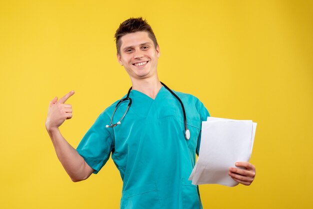 Vista frontal de um médico em terno médico com análise sorrindo na parede amarela