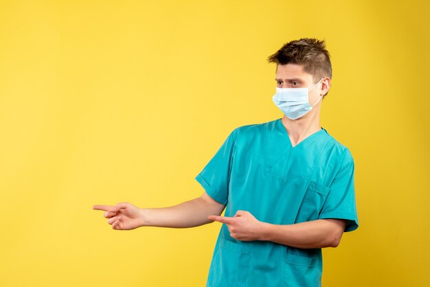Vista frontal de um médico em terno médico com máscara estéril na parede amarela