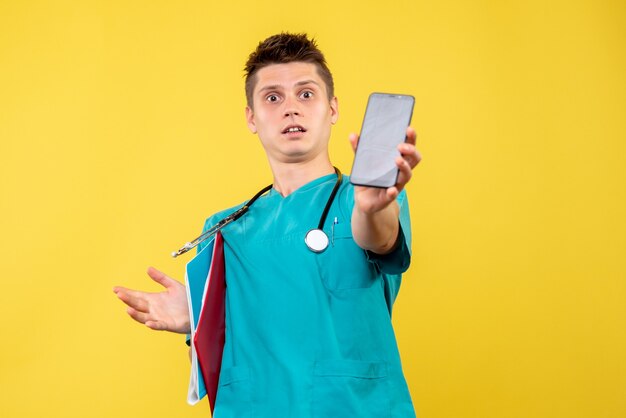 Vista frontal de um médico em terno médico com telefone e nota na parede amarela
