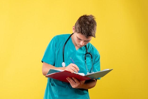 Vista frontal de um médico em terno médico segurando uma análise na parede amarela