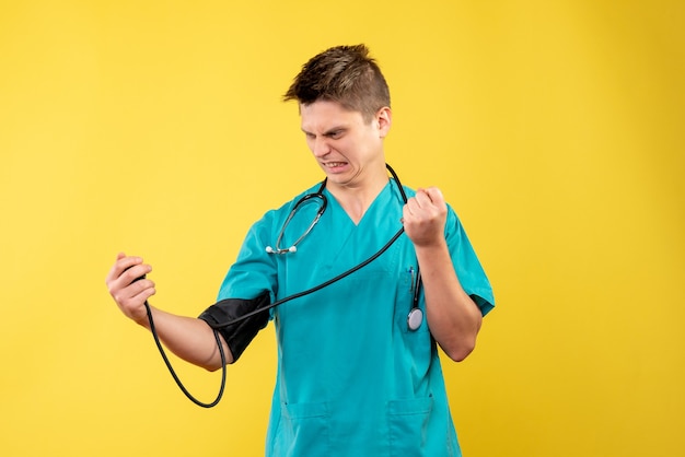 Vista frontal de um médico em terno médico, verificando sua pressão na parede amarela