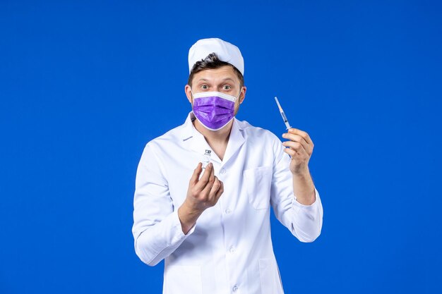 Vista frontal de um médico em traje médico e máscara com injeção e vacina em azul