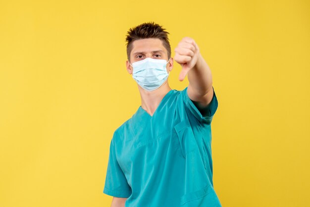 Vista frontal de um médico em traje médico e máscara estéril na parede amarela