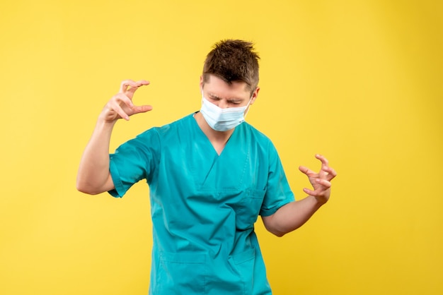 Vista frontal de um médico em traje médico e máscara estéril na parede amarela