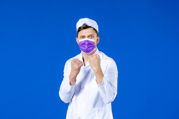 Vista frontal de um médico em traje médico e máscara roxa em boxe azul