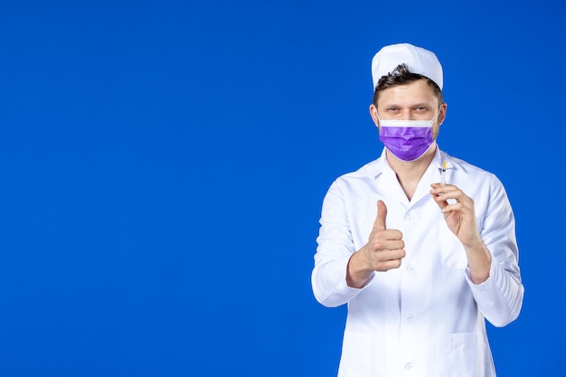 Vista frontal de um médico em traje médico e máscara roxa segurando injeção em azul