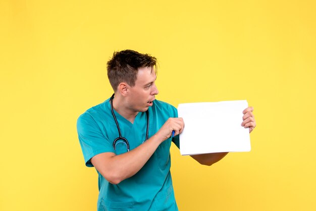 Vista frontal de um médico segurando arquivos na parede amarela