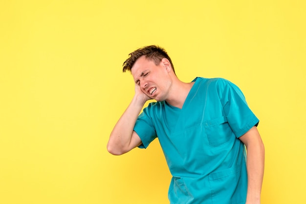 Vista frontal de um médico sofrendo de dor de cabeça na parede amarela