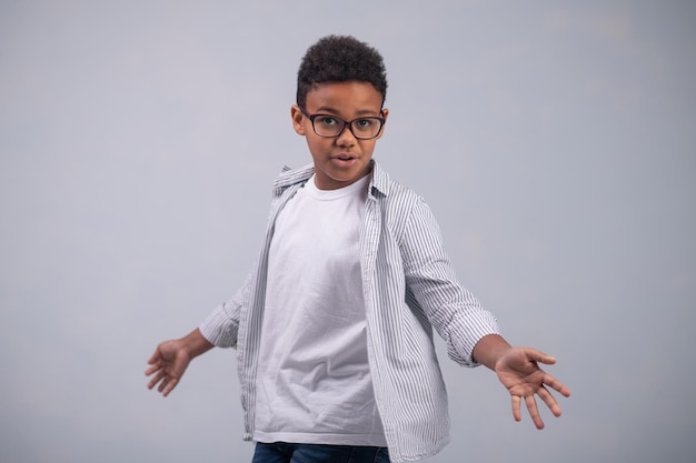 Vista frontal de um menino de óculos mostrando as palmas das mãos abertas diante da câmera