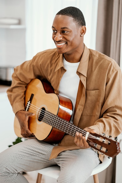 Vista frontal de um músico sorridente em casa tocando violão