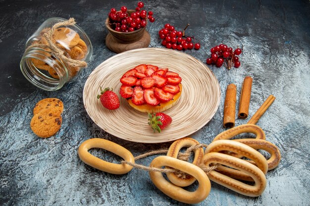 Vista frontal de um pequeno bolo de frutas com biscoitos na superfície escura