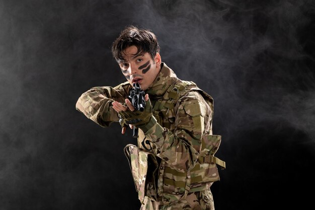 Vista frontal de um soldado camuflado com o rifle mirando na parede escura