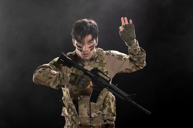 Vista frontal de um soldado lutando durante uma operação com um rifle na parede escura