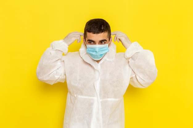 Vista frontal de um trabalhador científico do sexo masculino em traje de proteção especial, usando sua máscara na parede amarela
