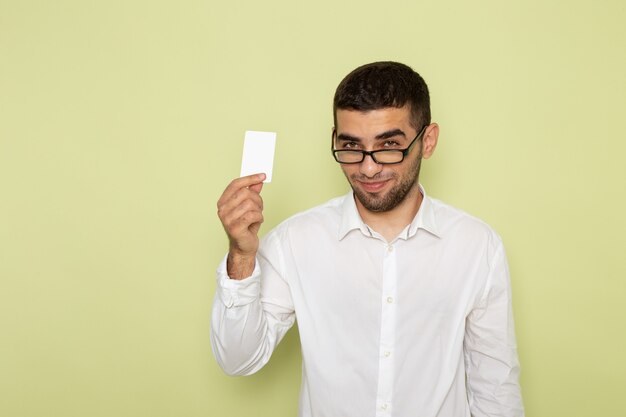 Vista frontal de um trabalhador de escritório com camisa branca segurando um cartão com um sorriso na parede verde-clara