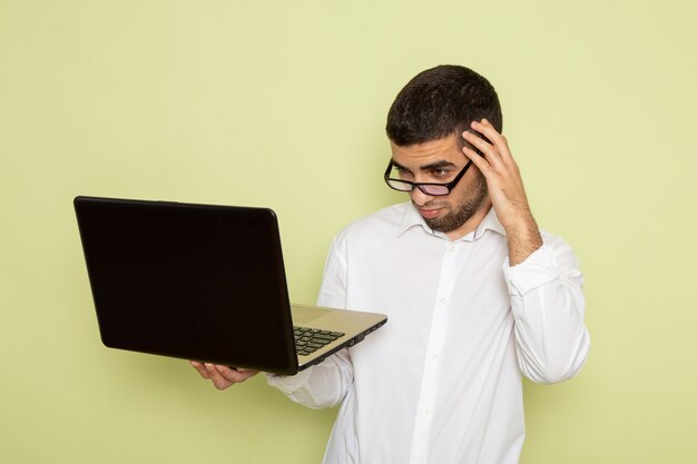 Foto grátis vista frontal de um trabalhador de escritório do sexo masculino com camisa branca usando seu laptop na parede verde-clara