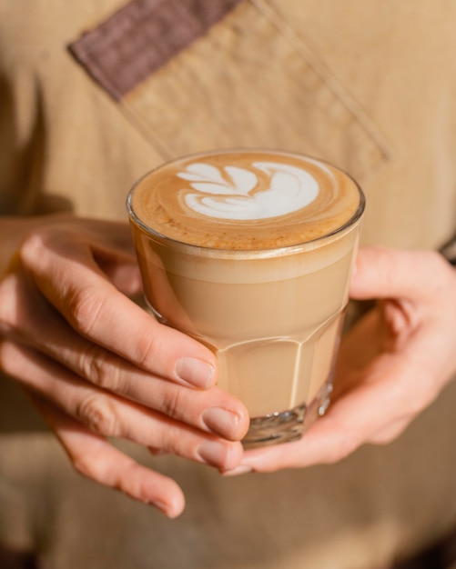 Vista frontal de uma barista com avental segurando um copo de café decorado