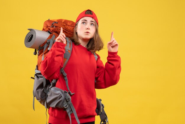 Vista frontal de uma bela viajante feminina com mochila apontando com os dedos para cima