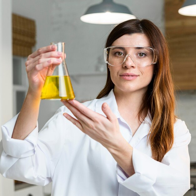 Vista frontal de uma cientista segurando um tubo de ensaio e usando óculos de segurança