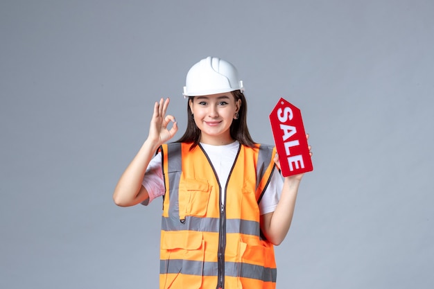 Vista frontal de uma construtora segurando uma placa vermelha de venda na parede branca