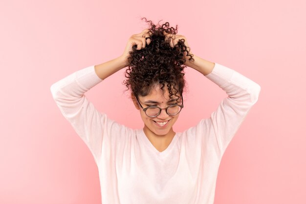 Vista frontal de uma jovem brincando com seu cabelo na parede rosa