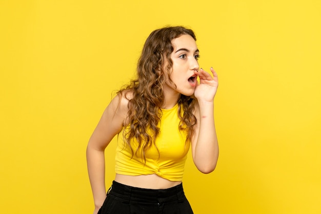 Vista frontal de uma jovem chamando com um sussurro na parede amarela