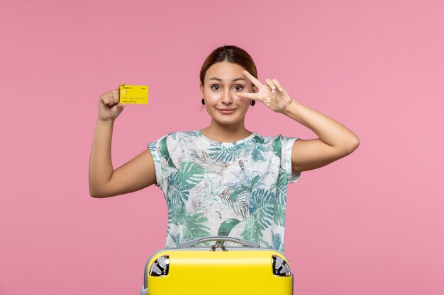 Vista frontal de uma jovem com cartão amarelo e bolsa na parede rosa