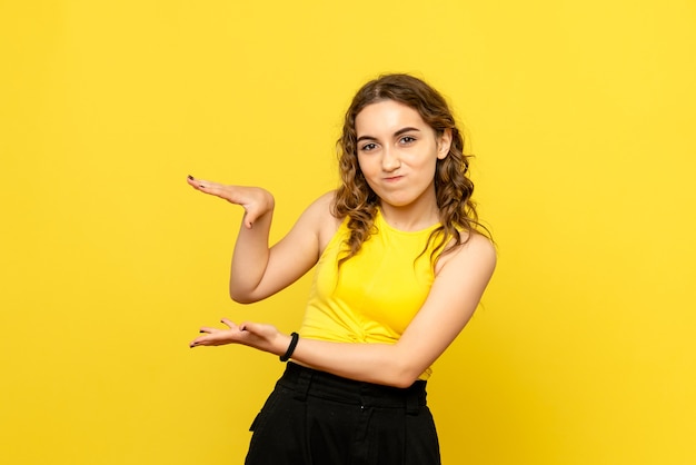 Vista frontal de uma jovem com expressão confusa na parede amarela
