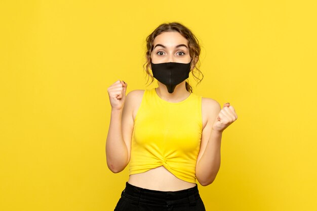 Vista frontal de uma jovem com máscara estéril na parede amarela