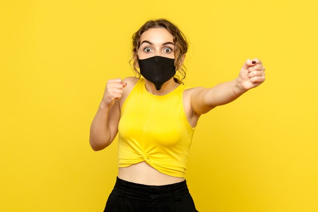 Vista frontal de uma jovem com máscara na parede amarela