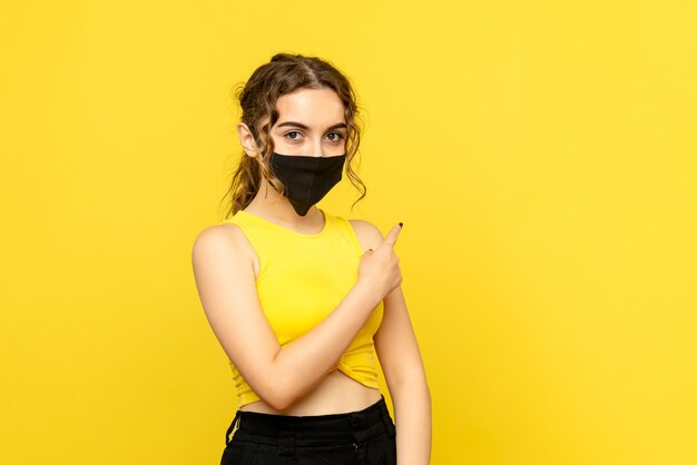 Vista frontal de uma jovem com máscara na parede amarela