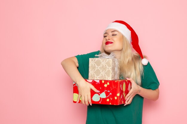 Vista frontal de uma jovem com presentes de Natal na parede rosa