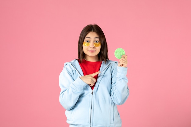 Vista frontal de uma jovem com tapa-olhos e uma pequena esponja na parede rosa