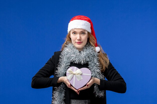 Vista frontal de uma jovem com um presente de ano novo na parede azul