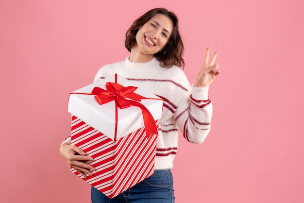 Vista frontal de uma jovem com um presente de Natal sorrindo na parede rosa