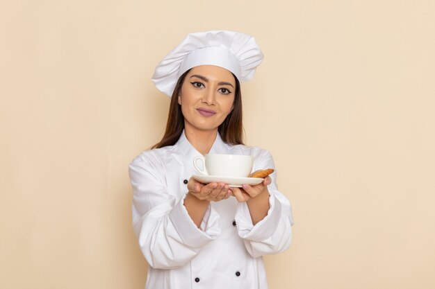 Vista frontal de uma jovem cozinheira em um terno branco segurando uma xícara de café na parede branca