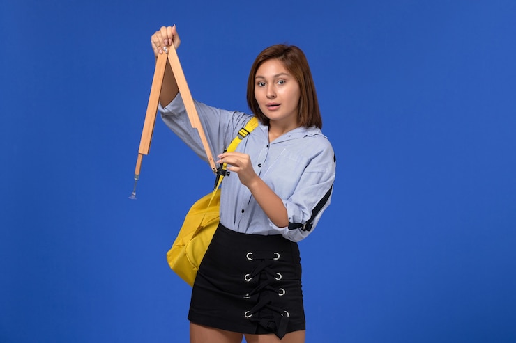 Foto grátis vista frontal de uma jovem de camisa azul segurando uma forma de madeira na parede azul