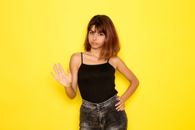 Vista frontal de uma jovem de camisa preta, apenas posando na parede amarelo-claro