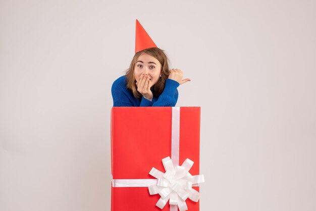 Vista frontal de uma jovem dentro de uma caixa de presente vermelha na parede branca
