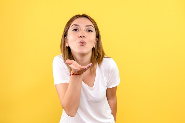 Vista frontal de uma jovem mandando beijos no ar na parede amarela