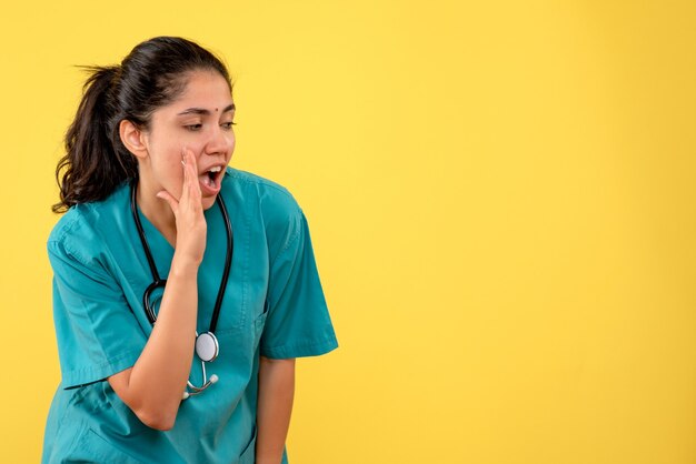 Vista frontal de uma jovem médica ligando para alguém na parede amarela