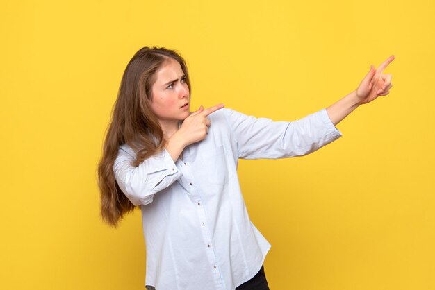 Vista frontal de uma jovem mulher apontando para uma parede amarela