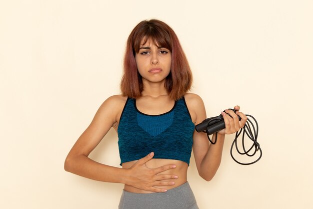 Vista frontal de uma jovem mulher com corpo em forma de camisa azul, segurando cordas de pular na parede branca