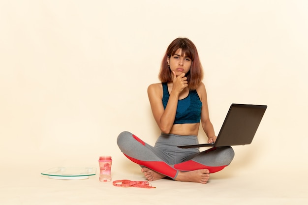 Vista frontal de uma jovem mulher com corpo em forma de camisa azul usando laptop na parede branca