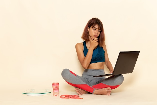 Vista frontal de uma jovem mulher com corpo em forma de camisa azul usando laptop na parede branca